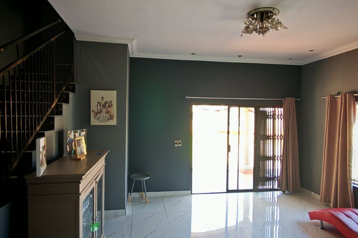 Spacious living room featuring modern tiled flooring, a sleek staircase with metal balustrade, and direct access to the outdoor area via sliding glass doors.