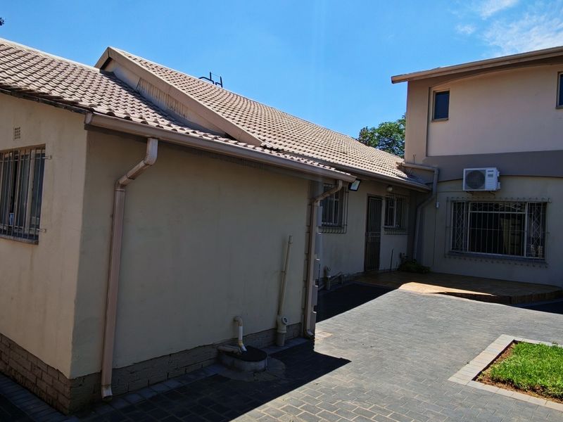 Rear exterior view of the property featuring a paved courtyard, tiled roof, and security-fitted windows.