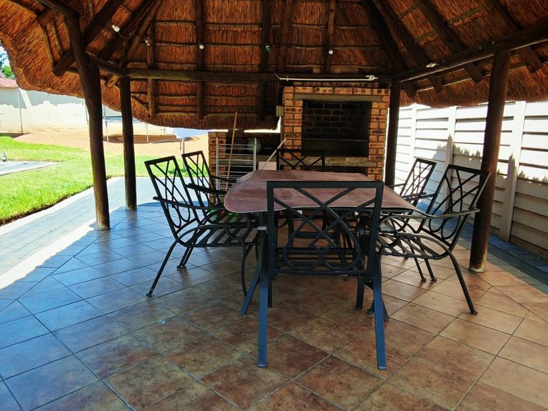 Covered outdoor patio area featuring a traditional thatched roof, built-in brick braai, and tiled flooring, ideal for outdoor entertaining.