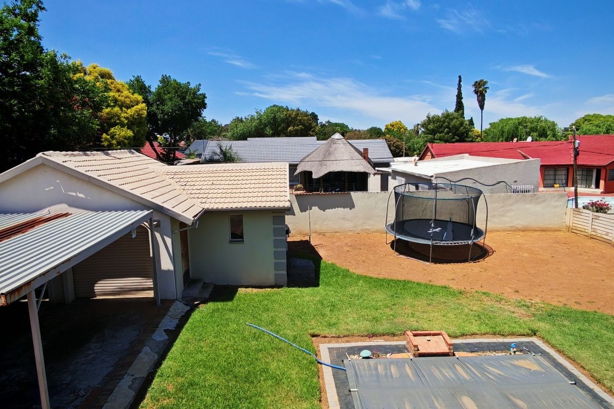 Aerial view of the property backyard featuring a swimming pool, lawn area, boundary wall, and a covered carport structure.