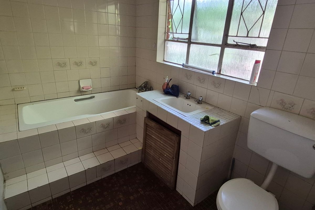 A dated bathroom featuring a built-in tiled bathtub, vanity with integrated basin, and toilet, requiring modernization of finishes and fixtures.