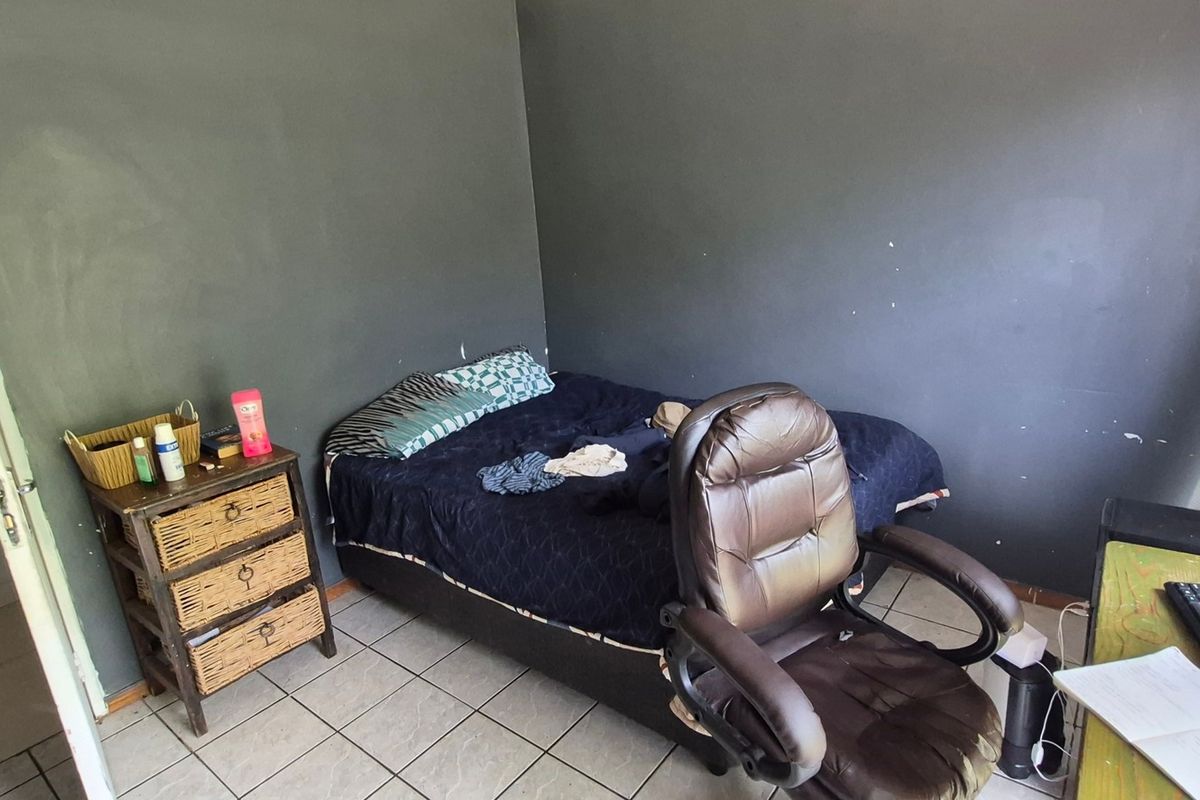A bedroom featuring tiled flooring and dark painted walls, showing signs of wear and tear on the wall surfaces.