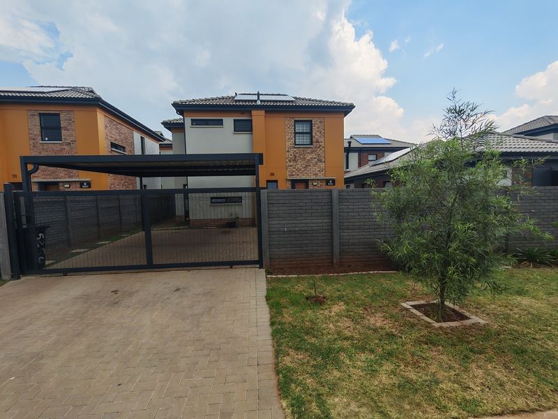 Front exterior view of a modern double-story house featuring a paved driveway, carport, secure sliding gate, and brick boundary wall.