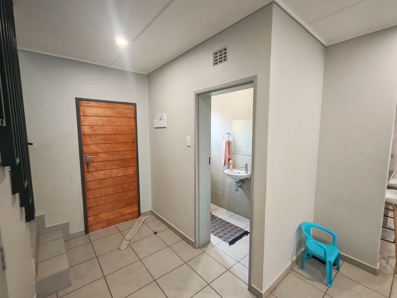 A clean, neutral-toned hallway featuring tiled flooring, a solid wooden door, and direct access to an adjacent bathroom.