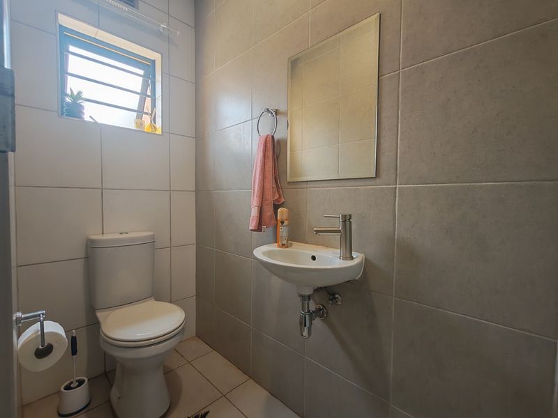 A compact, modern bathroom featuring a wall-mounted basin, toilet, and neutral tiled finishes, providing a clean and functional space.