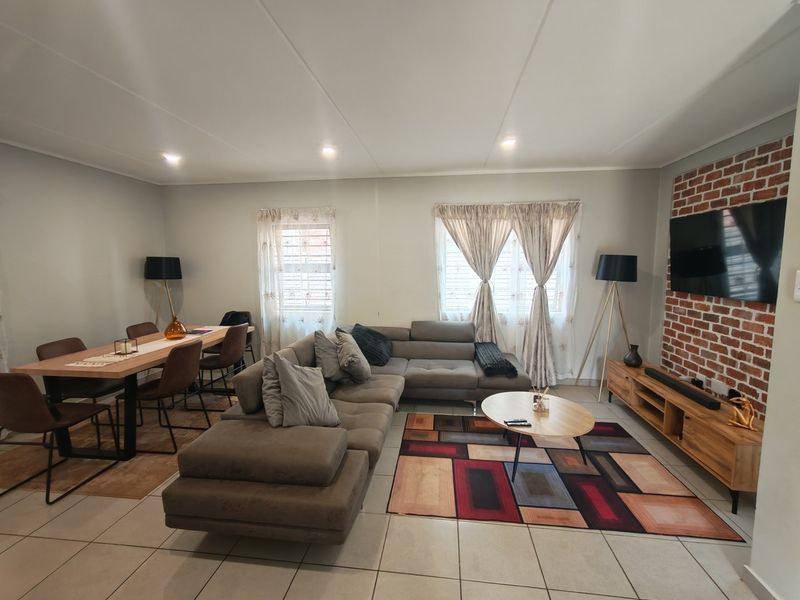 Spacious open-plan living and dining area featuring tiled flooring, recessed lighting, and a distinctive exposed brick feature wall.