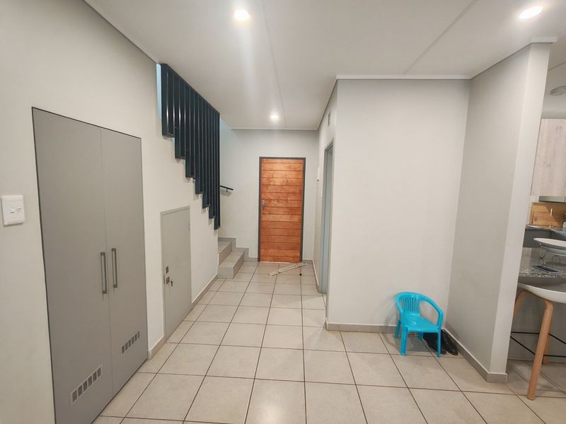 A bright and modern entrance hall featuring tiled flooring, a built-in storage cupboard, and a staircase with a contemporary metal balustrade.