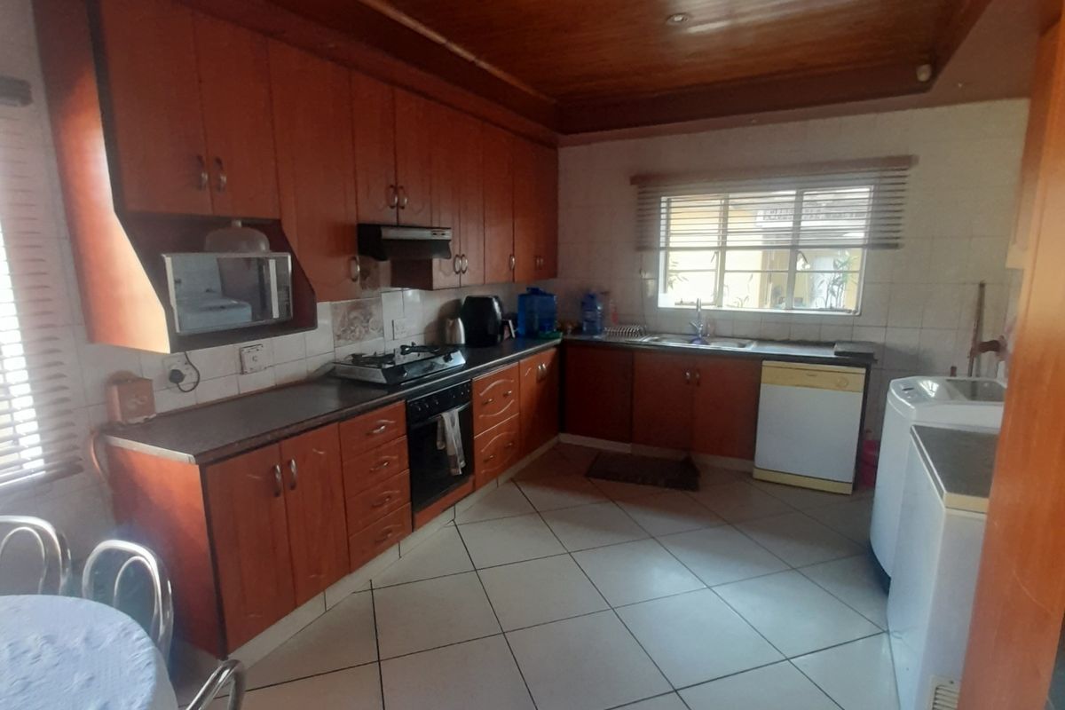 A functional kitchen featuring wooden cabinetry, a gas hob with extractor, built-in oven, double sink, and tiled flooring with a warm wooden ceiling finish.