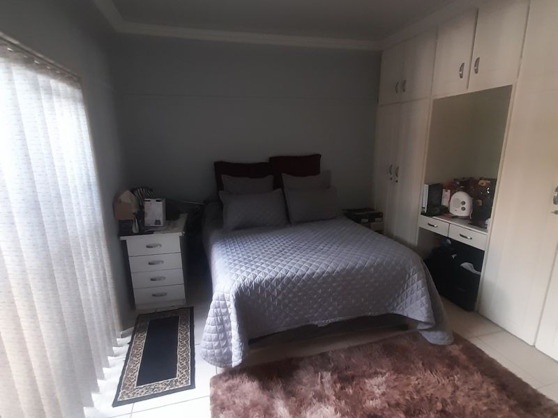 A bedroom featuring built-in cupboards, tiled flooring, and vertical blinds, offering a functional space with neutral finishes.