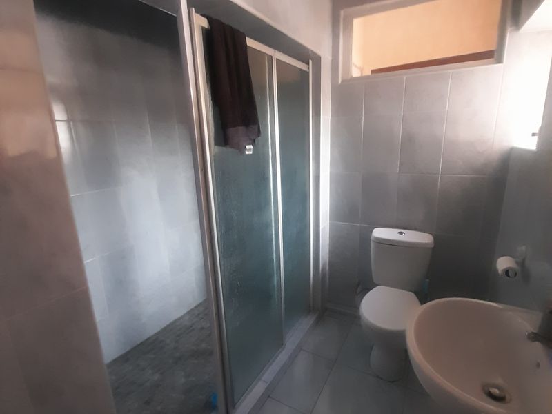 A functional bathroom featuring a shower enclosure, pedestal basin, and toilet, finished with neutral wall and floor tiling.