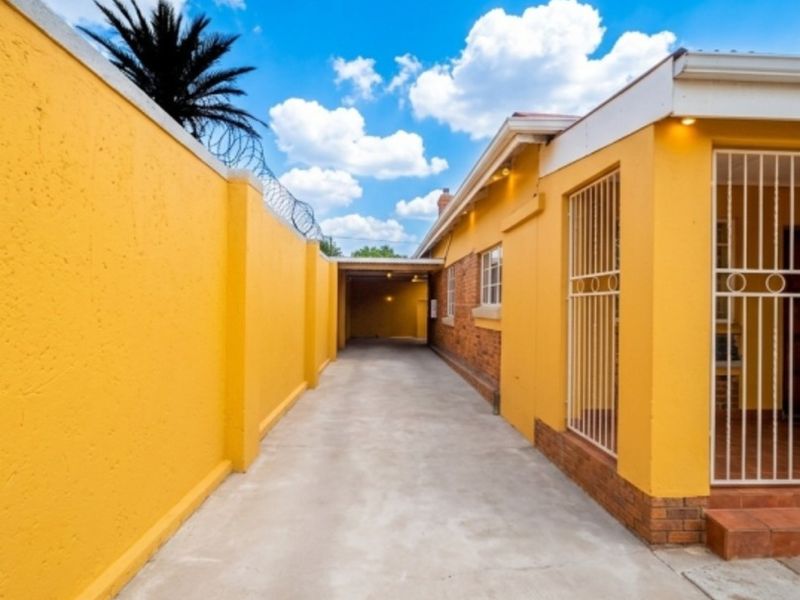 A well-maintained exterior driveway featuring a concrete surface, perimeter wall with security fencing, and a covered carport area.