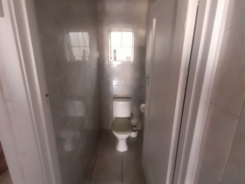 A compact, tiled bathroom featuring a standard toilet and a small window, providing a functional and clean utility space.