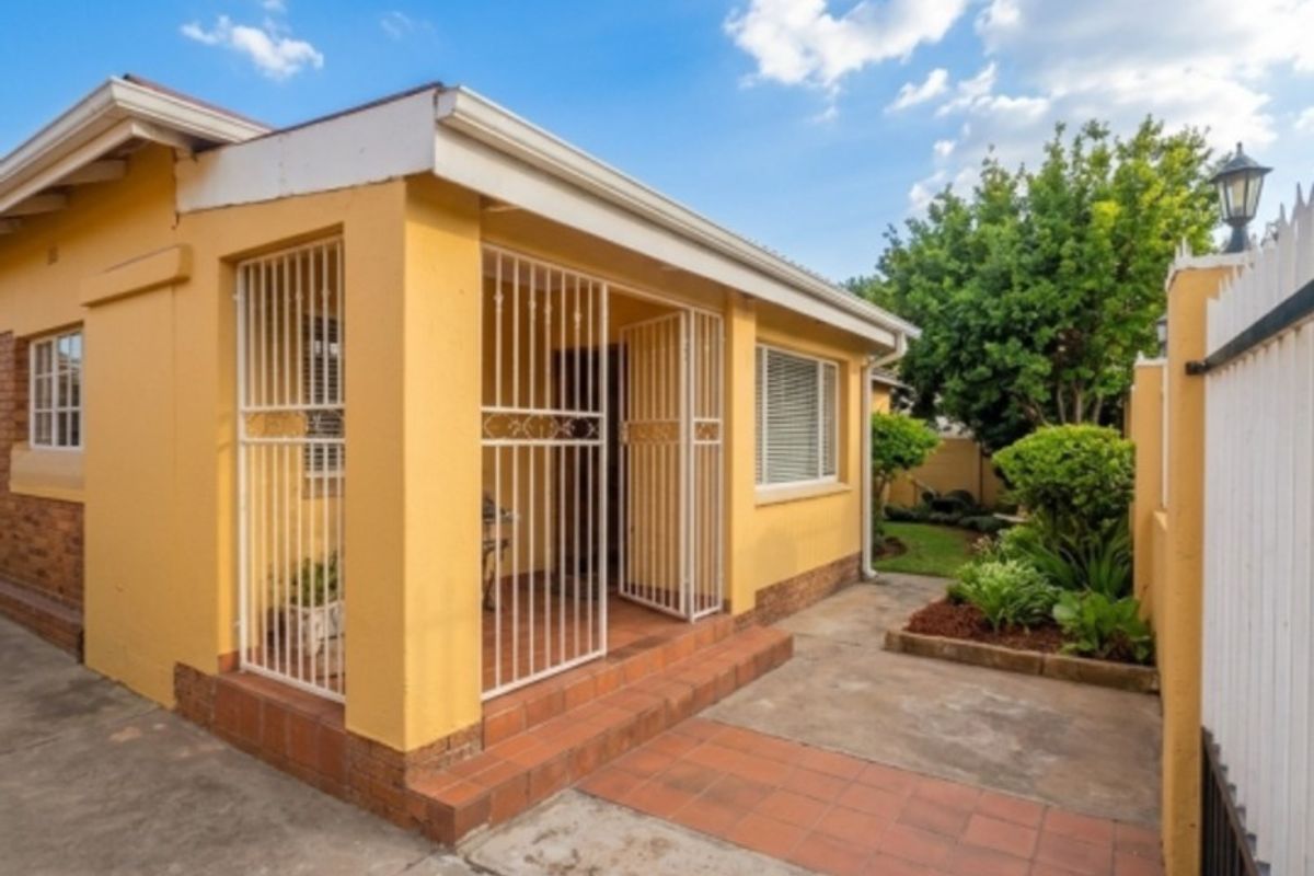 Rear exterior view of the property featuring a covered patio area, tiled walkway, and a small garden space with perimeter fencing.