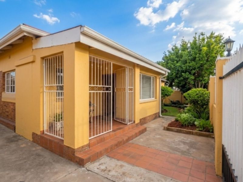 Rear exterior view of the property featuring a covered patio area, tiled walkway, and a small garden space with perimeter fencing.