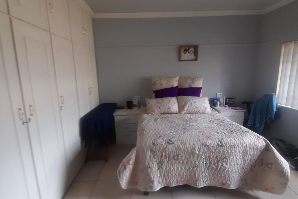 A bedroom featuring tiled flooring and extensive built-in cupboard storage, offering a functional and neutral space.
