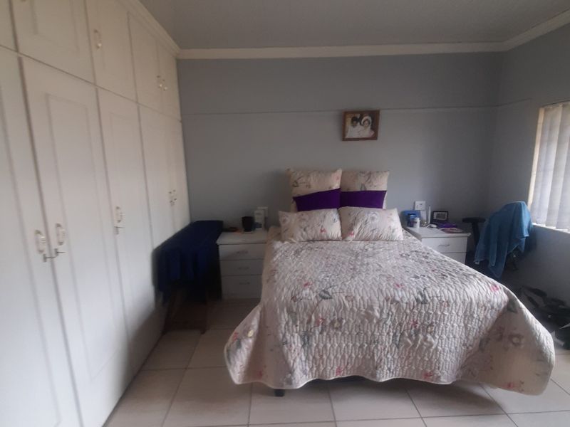 A bedroom featuring tiled flooring and extensive built-in cupboard storage, offering a functional and neutral space.