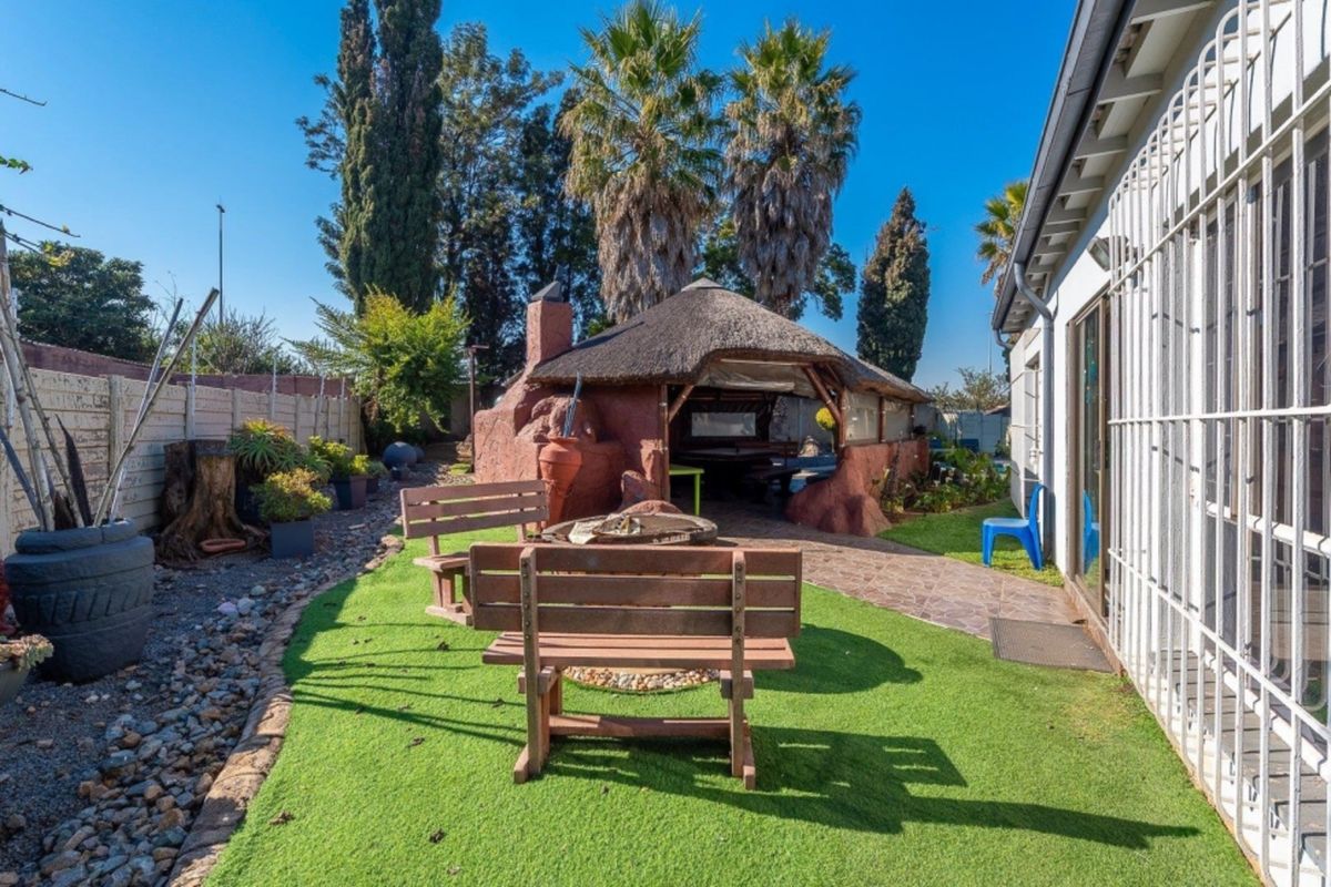 Rear garden area featuring an artificial lawn, paved pathway, and a traditional thatched lapa with a built-in braai facility.