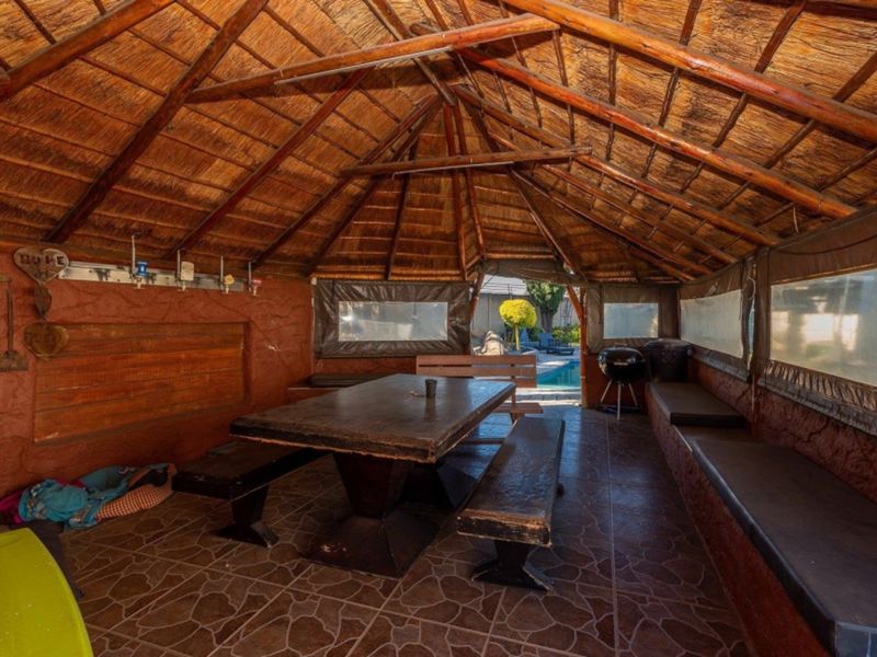 Covered outdoor entertainment area featuring a traditional thatched roof, exposed timber rafters, tiled flooring, and built-in bench seating, ideal for relaxed alfresco dining.