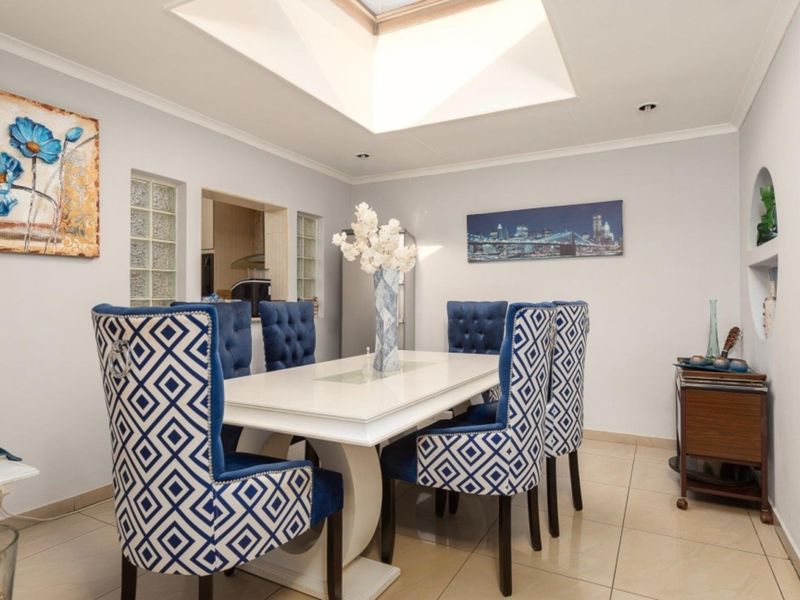 A bright dining room featuring tiled flooring, a central skylight, and decorative glass block wall inserts connecting to the adjacent kitchen area.