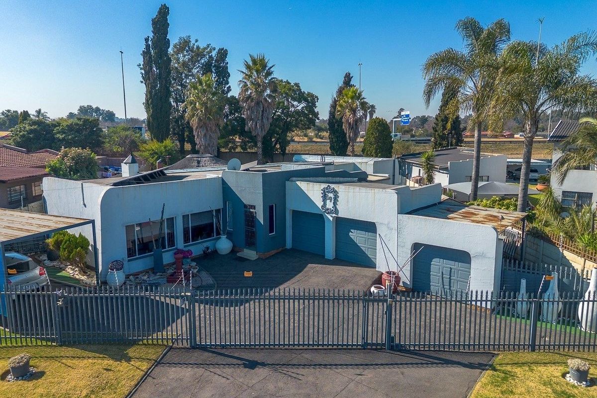 Aerial view of a residential property featuring a triple garage configuration, paved driveway, and secure perimeter fencing.