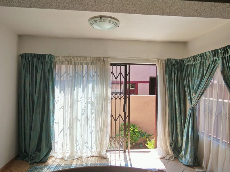 A bright, empty living room featuring tiled flooring, a sliding door with a security gate, and access to an outdoor area.