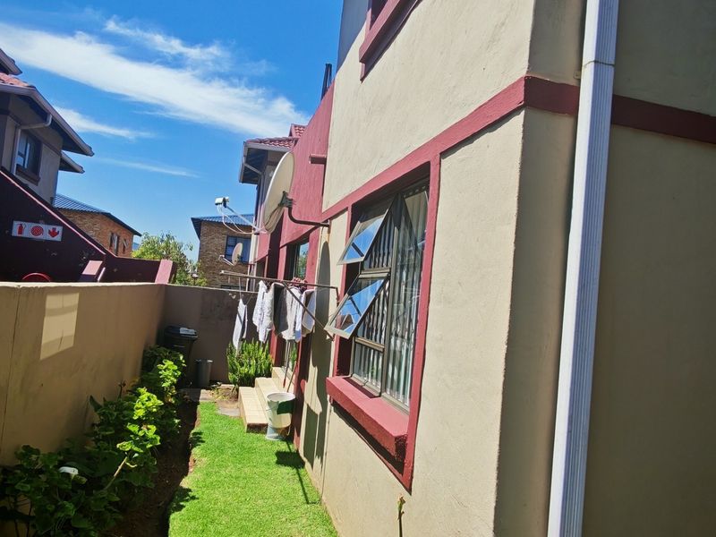 A view of the rear exterior of the townhouse, featuring a small garden area, boundary wall, and exterior window security bars.