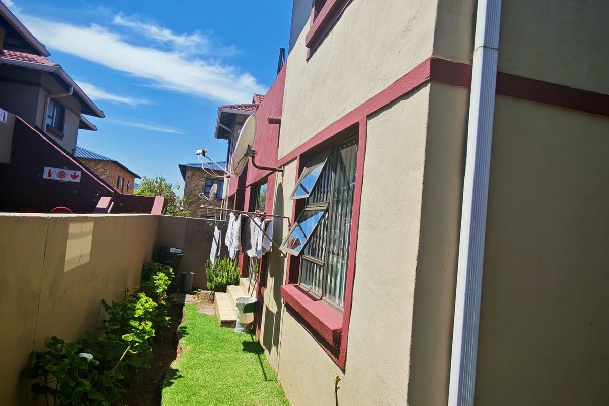 A view of the rear exterior of the townhouse, featuring a small garden area, boundary wall, and exterior window security bars.