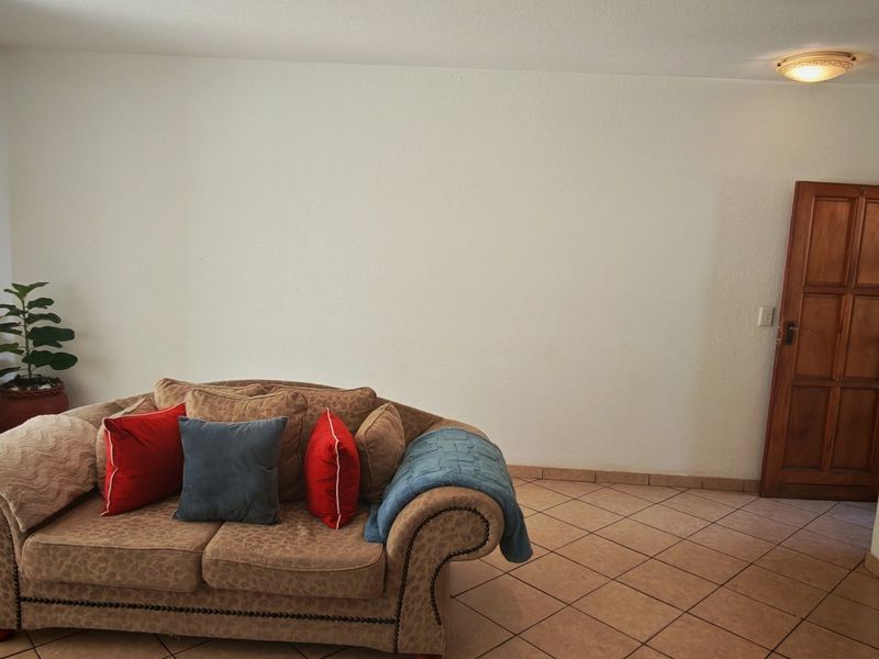 A living room area featuring ceramic floor tiles, a wooden door, and a flush mount ceiling light.