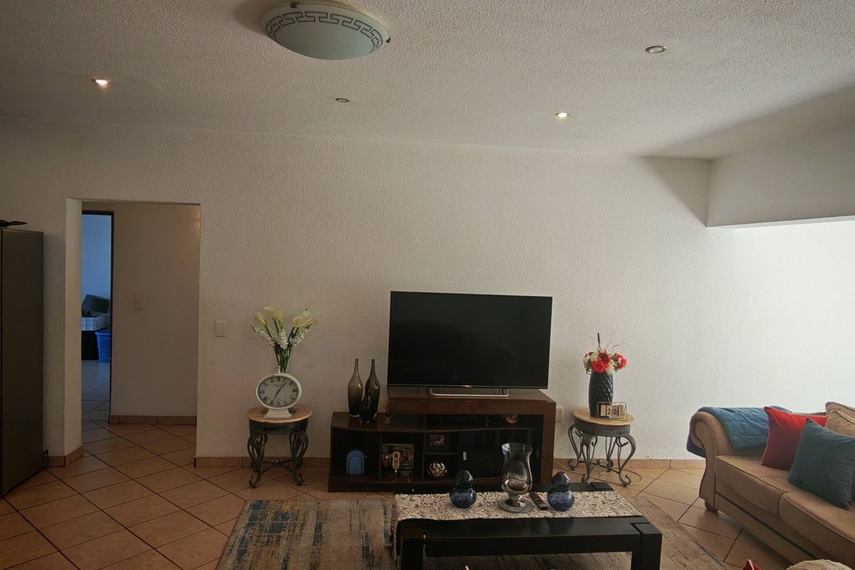 A living room featuring ceramic floor tiles, recessed downlights, and a textured ceiling, providing a functional and neutral space for relaxation.