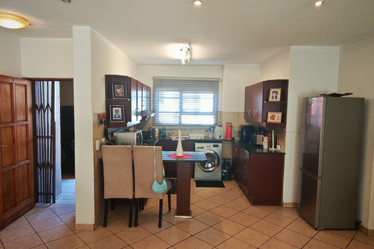 Functional kitchen featuring dark wood cabinetry, tiled flooring, integrated laundry appliances, and a breakfast bar area with direct access to adjacent rooms.