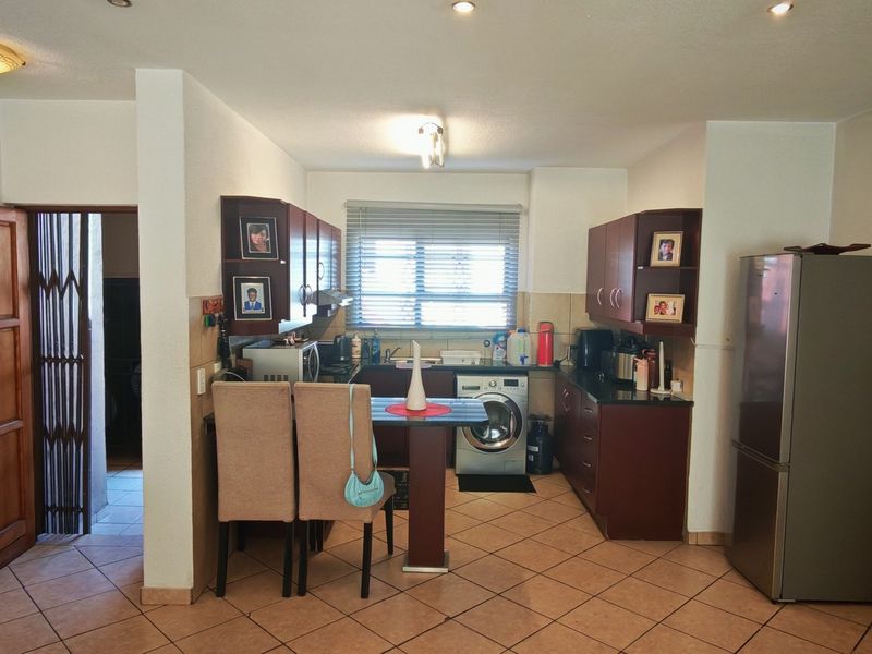 Functional kitchen featuring dark wood cabinetry, tiled flooring, integrated laundry appliances, and a breakfast bar area with direct access to adjacent rooms.