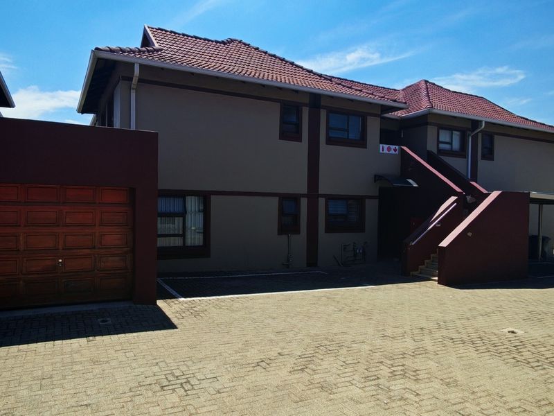 Front exterior view of a townhouse complex featuring a paved driveway, single garage, and external staircase leading to upper level units.