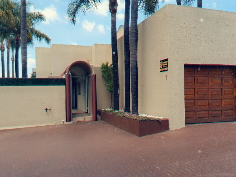 Front elevation of a townhouse featuring a double garage, paved driveway, and a distinct arched entrance with security gate.