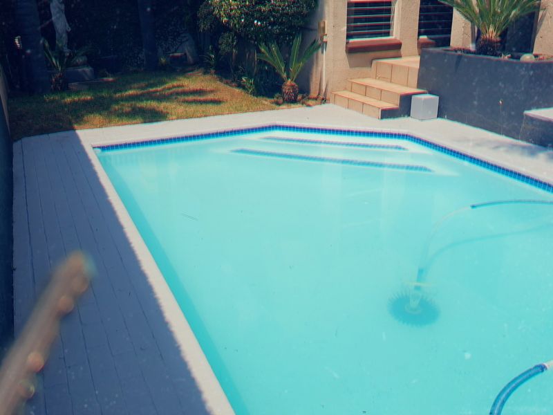 A private swimming pool area featuring a tiled surround, raised planter box, and adjacent lawn space, accessible via concrete steps.