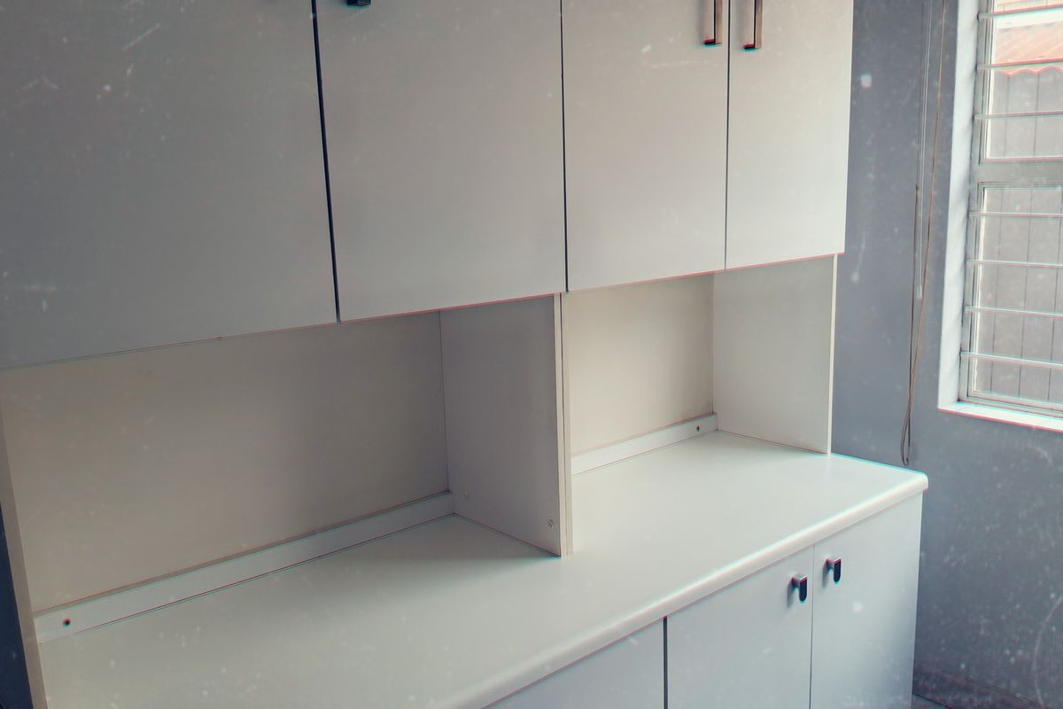A functional kitchen area featuring white built-in cabinetry, ample counter space, and a window with security bars.