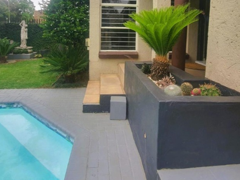 Outdoor pool area featuring a paved surround, built-in planter box, and tiled steps leading to the residence.
