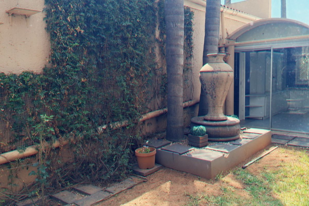 A rear garden area featuring a stone fountain, paved pathways, and sliding glass doors leading into the townhouse interior.