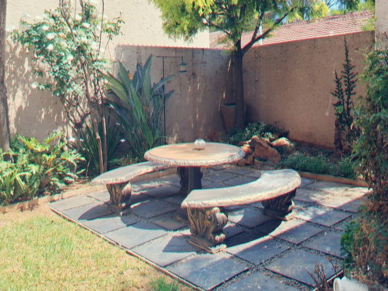 A private rear garden featuring a paved seating area, established trees, and perimeter boundary walls.