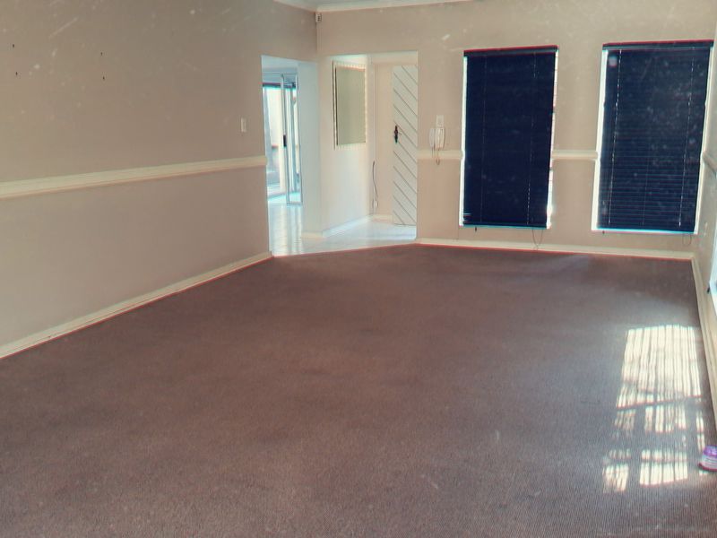 An empty living room featuring carpet flooring, chair rail molding, and dark venetian blinds, offering a blank canvas for potential interior updates.