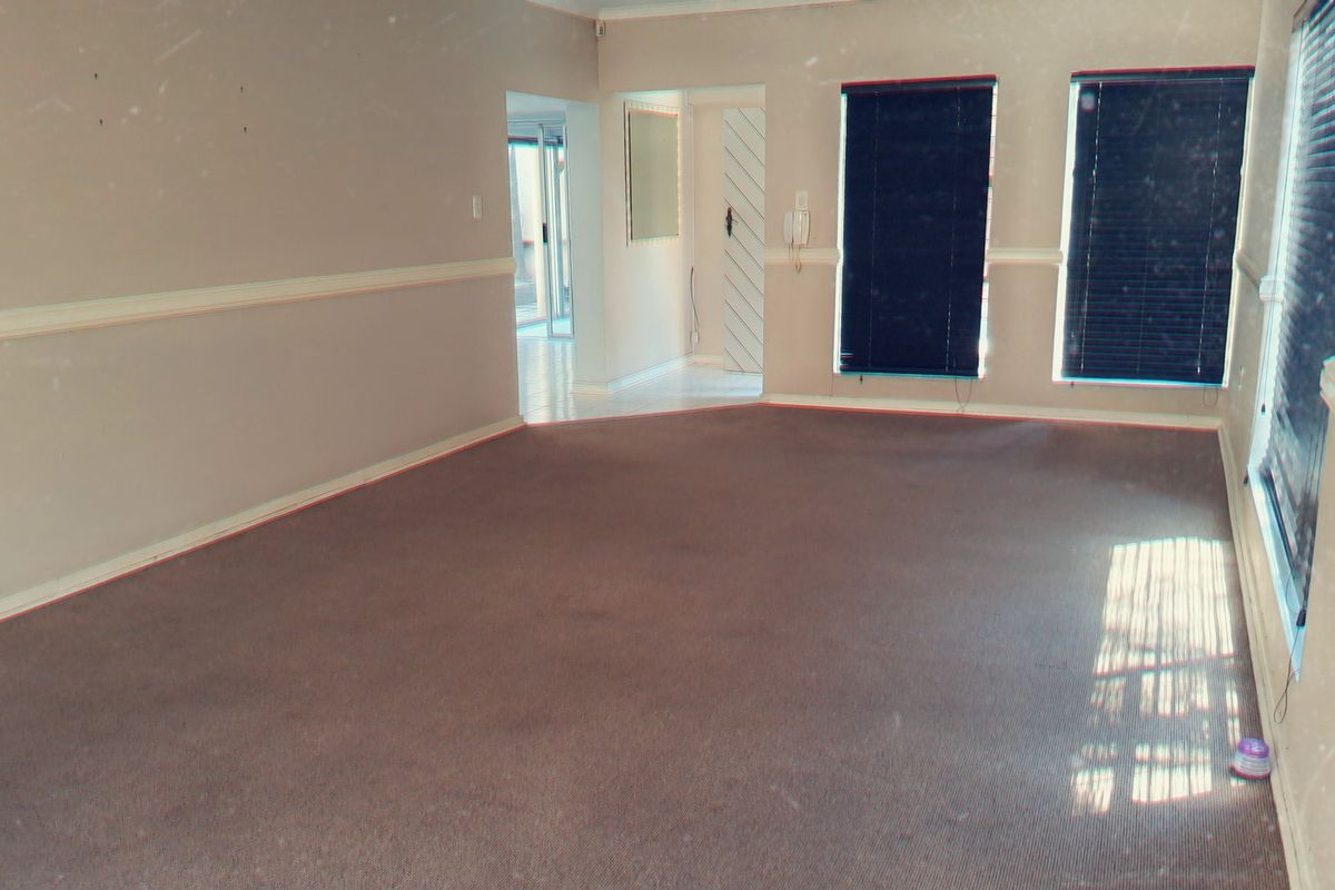 An empty living room featuring carpet flooring, chair rail molding, and dark venetian blinds, offering a blank canvas for potential interior updates.