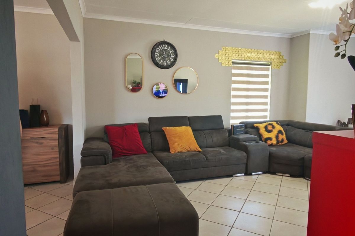 A comfortable living room featuring tiled flooring, neutral wall tones, and a window fitted with modern roller blinds.