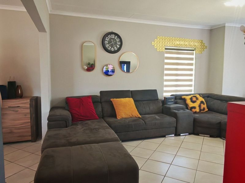 A comfortable living room featuring tiled flooring, neutral wall tones, and a window fitted with modern roller blinds.