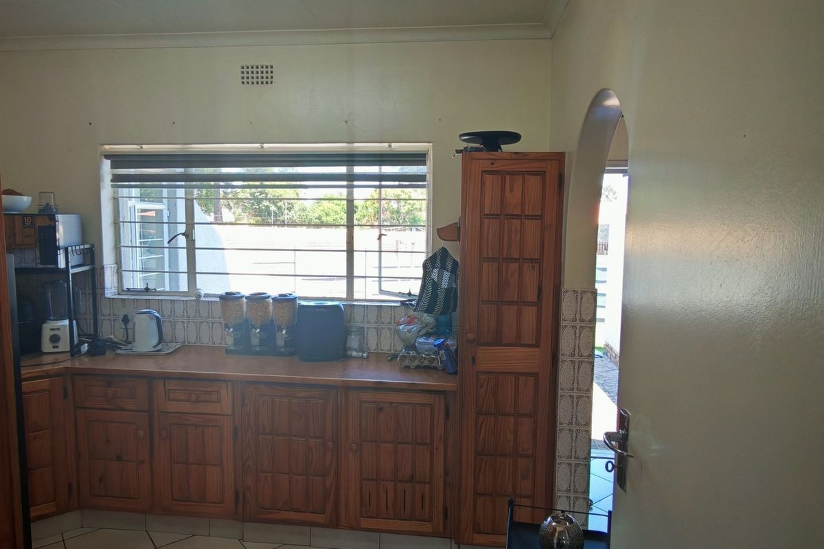 A functional kitchen featuring traditional wooden cabinetry, laminate countertops, and a tiled backsplash, with an arched doorway leading to an adjacent area.
