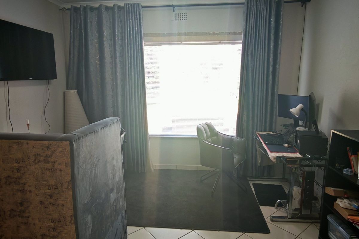 A functional bedroom space featuring tiled flooring and a large window with curtain rails, suitable for use as a bedroom or home office.