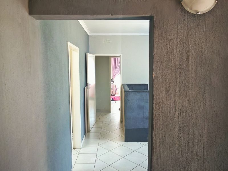 A view through a hallway featuring tiled flooring and textured grey walls, leading into adjacent living spaces.