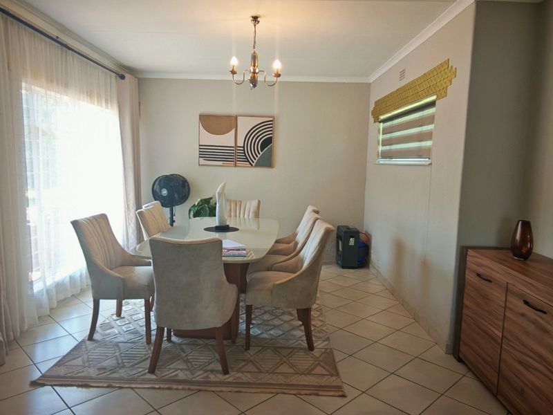 A well-lit dining room featuring tiled flooring, a central chandelier, and large windows that provide ample natural light.