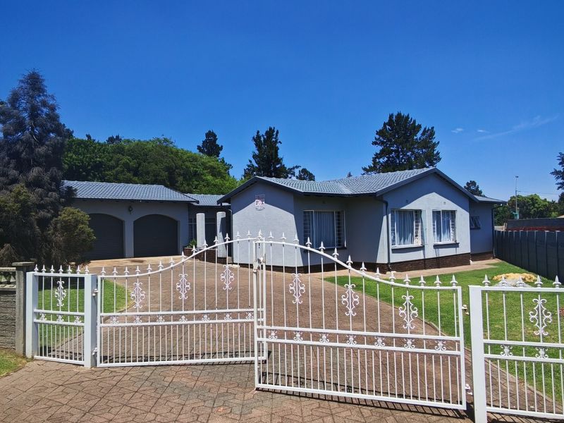 Front elevation of a single-story house featuring a paved driveway, secure wrought iron gate, and an attached double garage.
