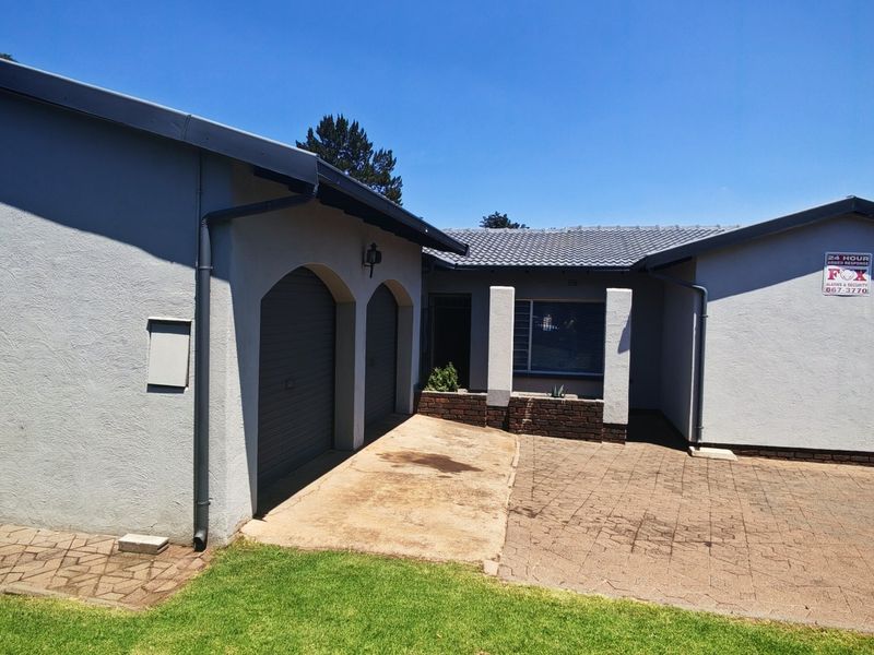 Front exterior view of the house featuring a double garage, paved driveway, and well-maintained facade with security alarm signage.