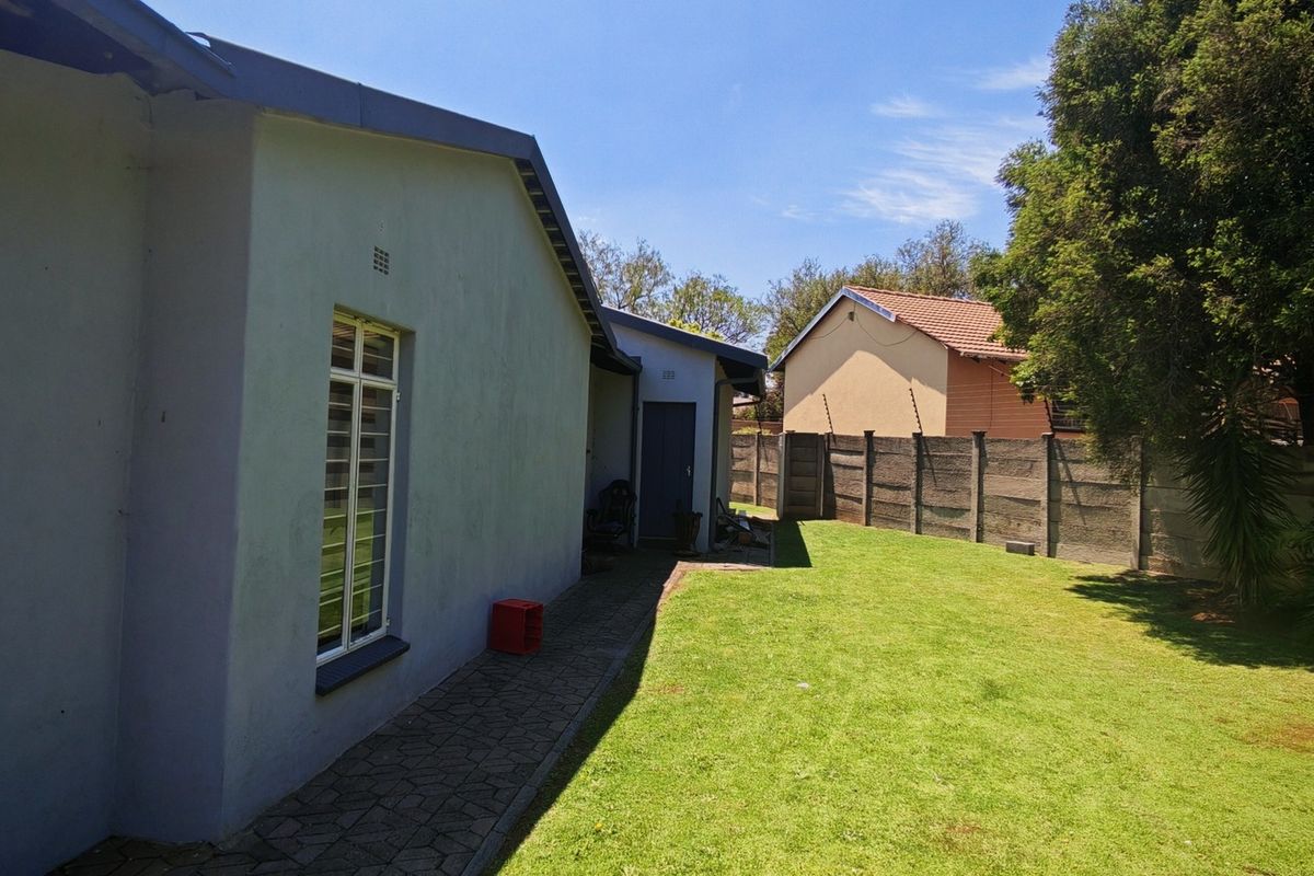 A view of the rear exterior of the house featuring a paved walkway, a well-maintained lawn, and a secure boundary wall.