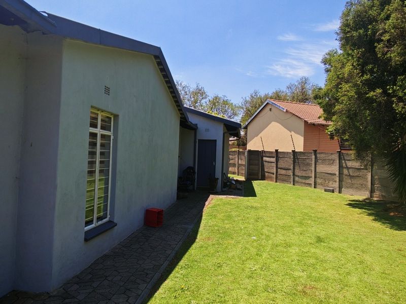 A view of the rear exterior of the house featuring a paved walkway, a well-maintained lawn, and a secure boundary wall.